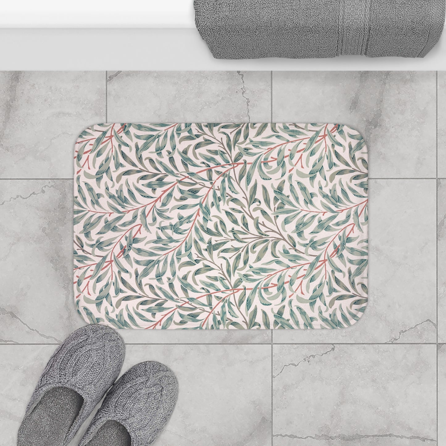 Floral-patterned bath mat on a tiled floor with slippers and a towel.