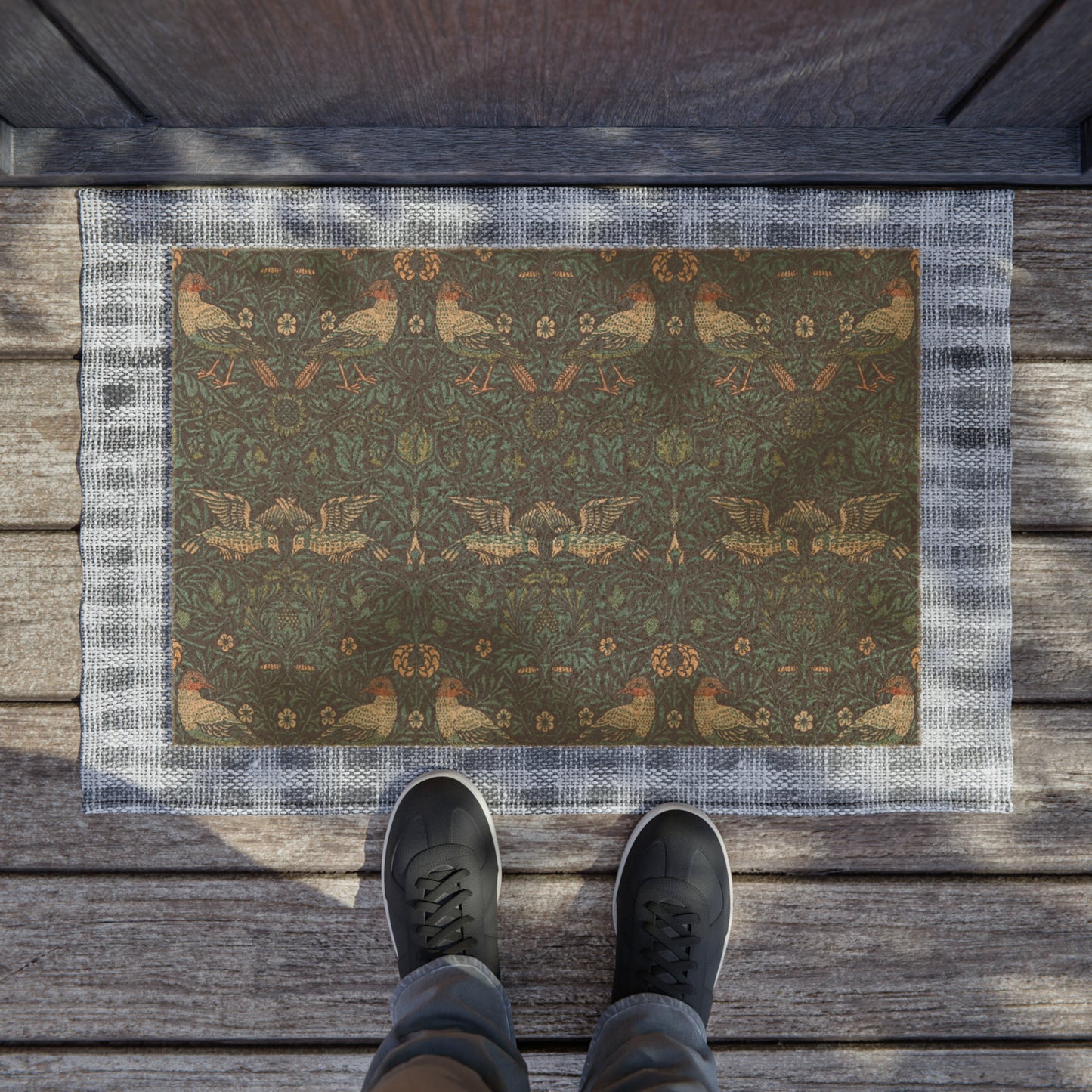 A rectangular coconut coir doormat with an intricate floral and animal pattern design, primarily in brown and green colours, with a black vinyl backing.