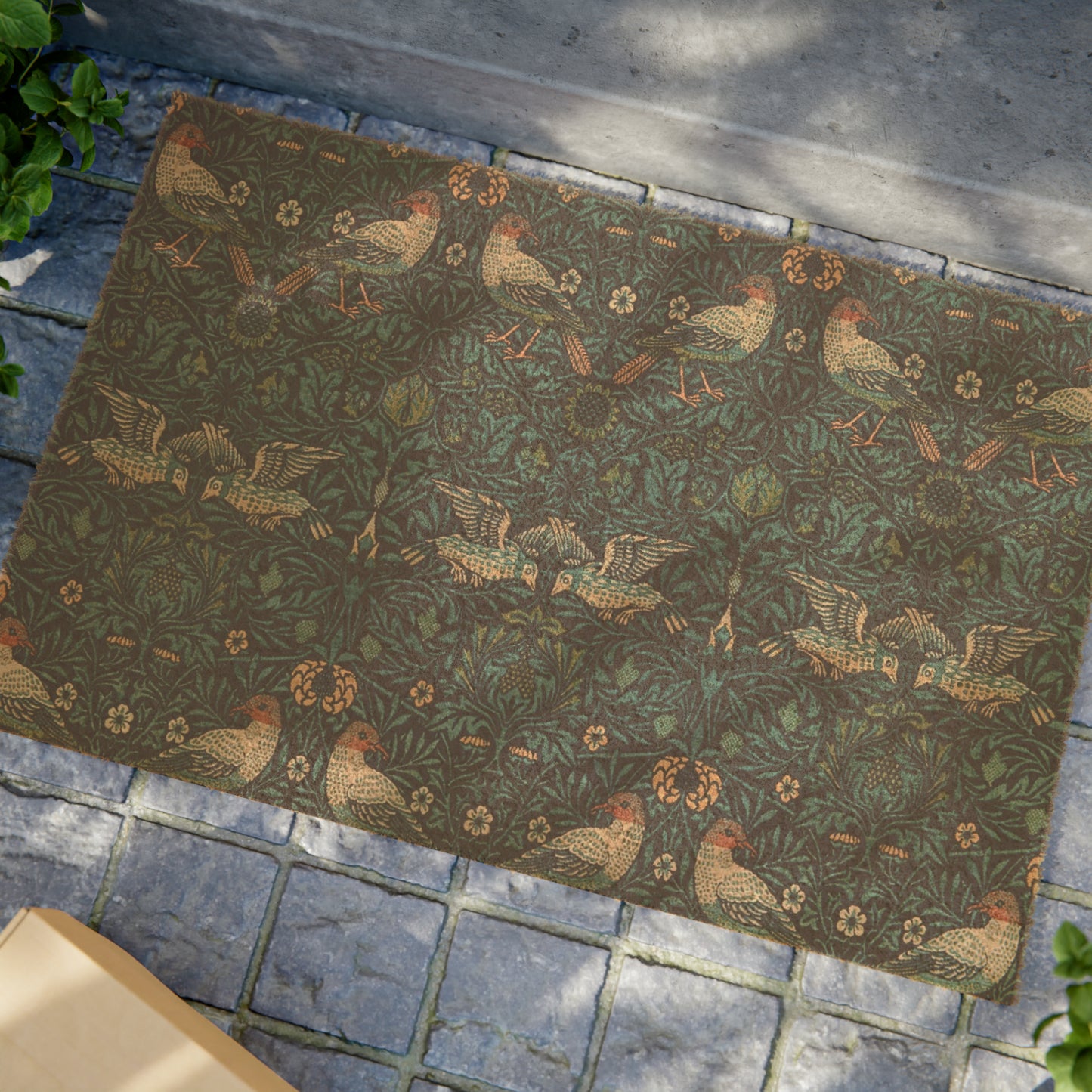 A rectangular coconut coir doormat with an intricate floral and animal pattern design, primarily in brown and green colours, with a black vinyl backing.