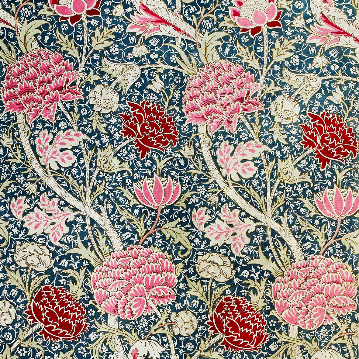 A floral patterned cotton twill napkin inspired by William Morris, displayed on a white plate with a piece of floral decor to the napkin's right.