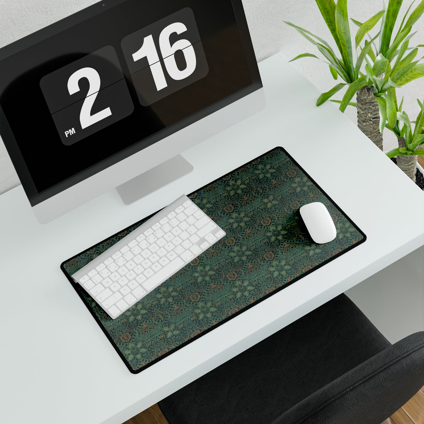 A rectangular desk mat with a William Morris & Co floral pattern in green, brown, and white, placed under a white desk and a keyboard.