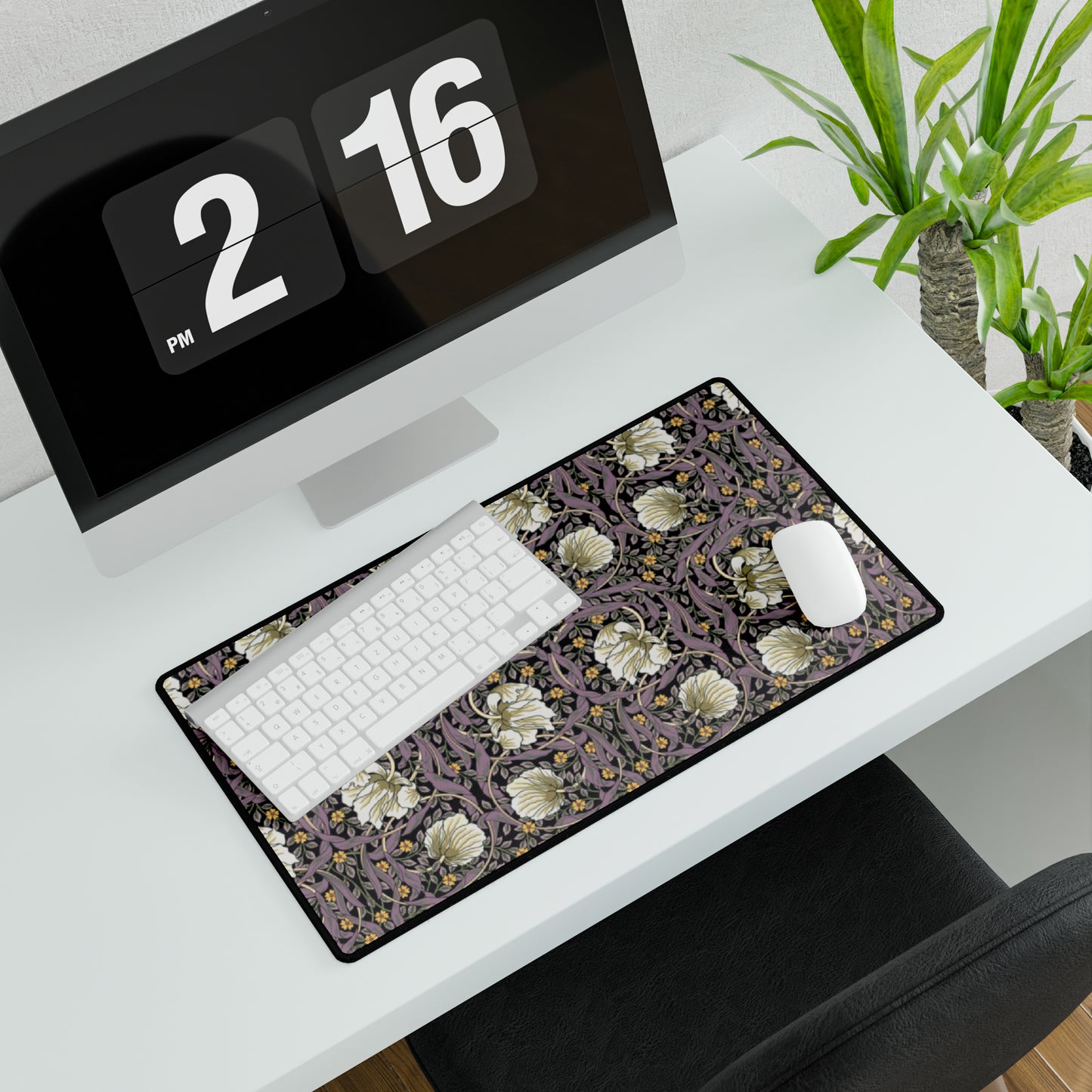A large desk mat with a William Morris & Co floral pattern, displayed on a desk with a keyboard and mouse, with a monitor above it showing a part of the mat.