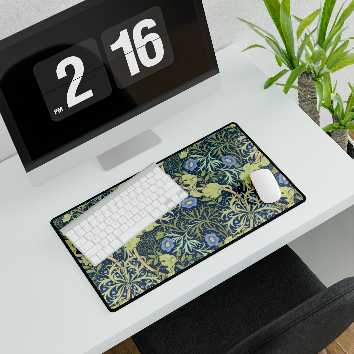 A large desk mat with a blue floral William Morris & Co pattern displayed under a monitor and accompanied by a keyboard and mouse.