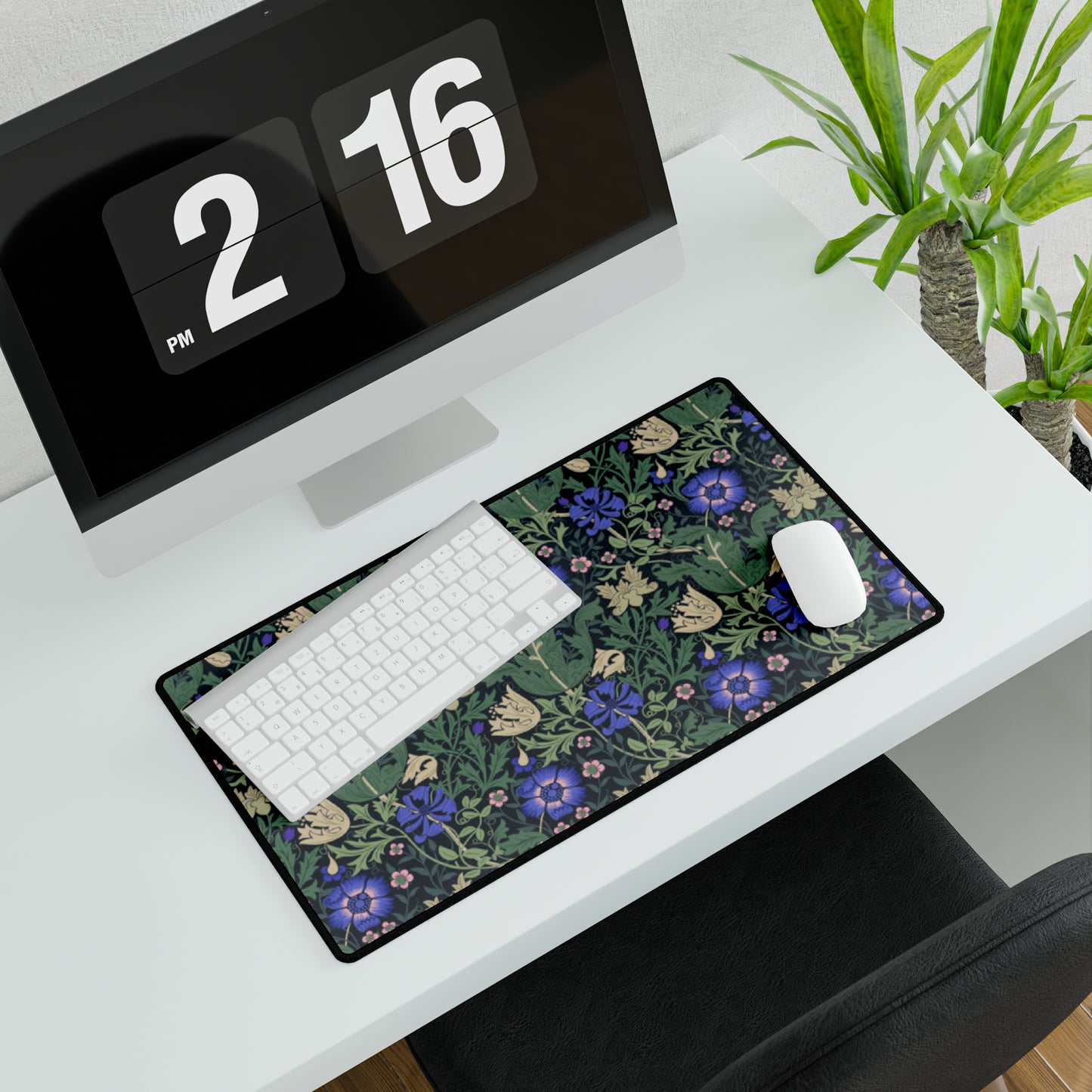 A desk mat with a William Morris & Co floral pattern, featuring a mouse pad on top. The desk mat has a non-slip base and is placed under a shelf with a computer monitor and a keyboard.