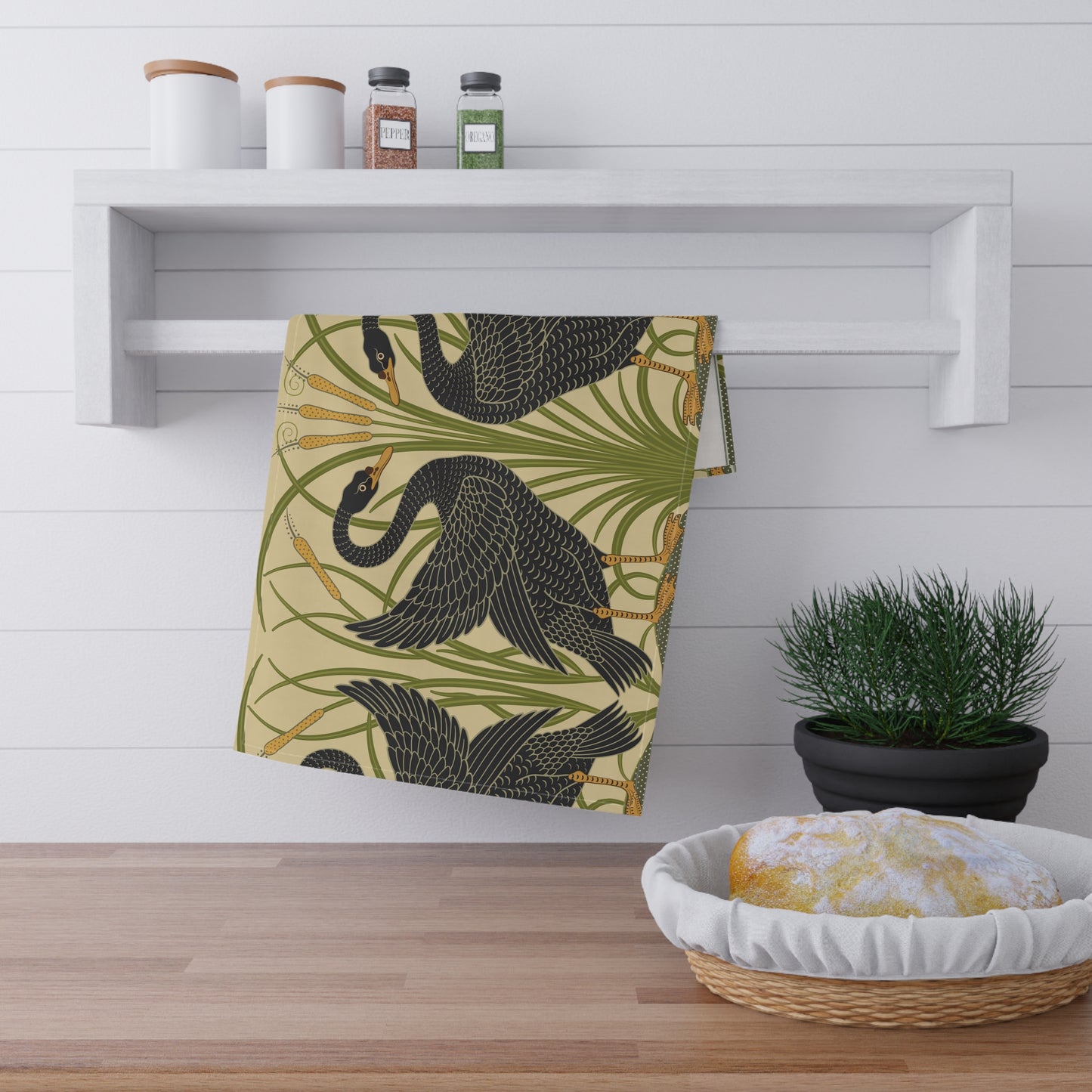 A kitchen tea towel with a repeating William Morris & Co pattern of black swans and green foliage on a beige background.