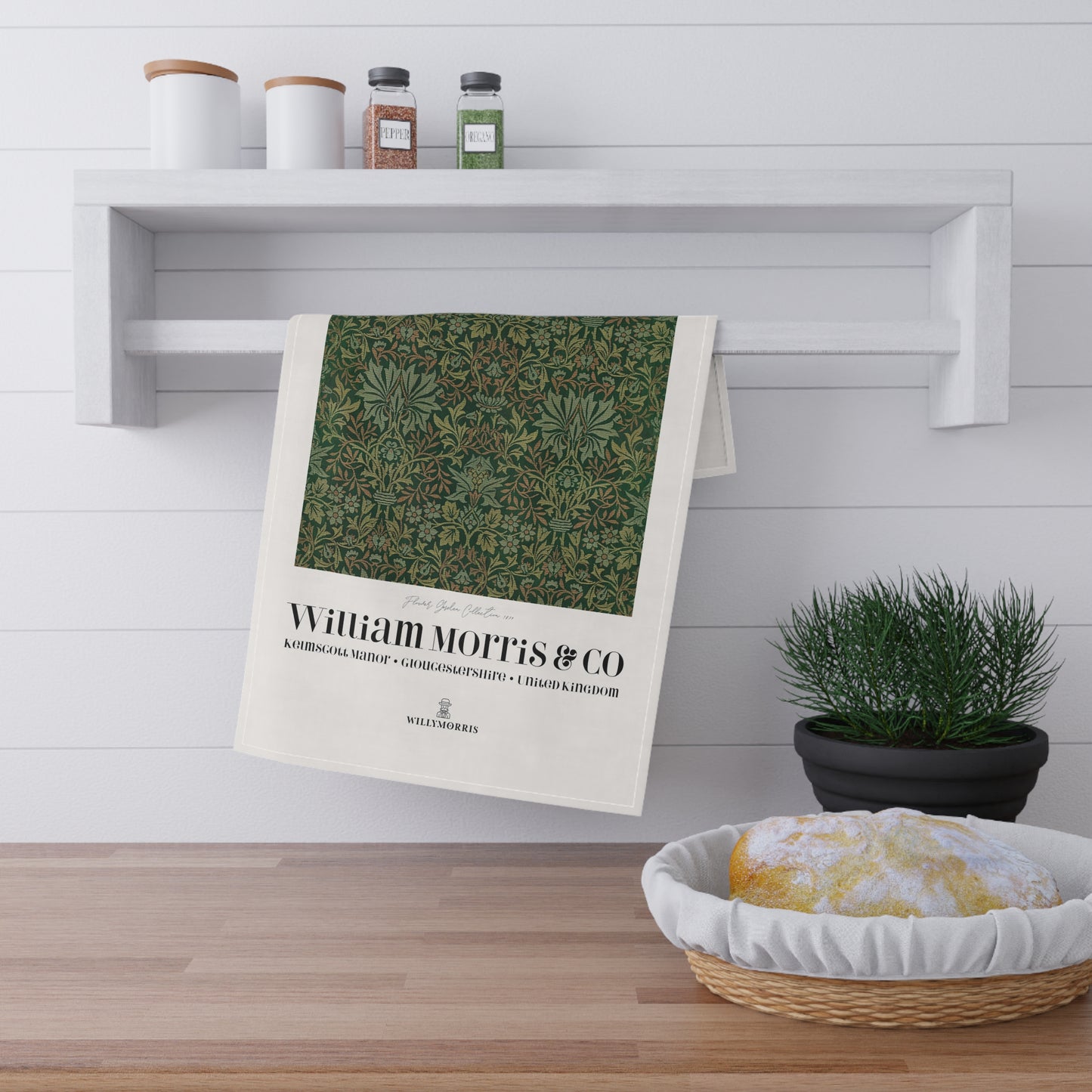 Tea towel with nature design and 'William Morris & Co' text hanging on a shelf.