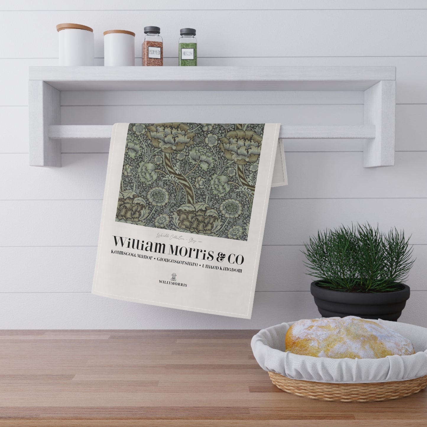 Decorative towel with 'William Morris & Co' design hanging on a shelf in a kitchen setting.