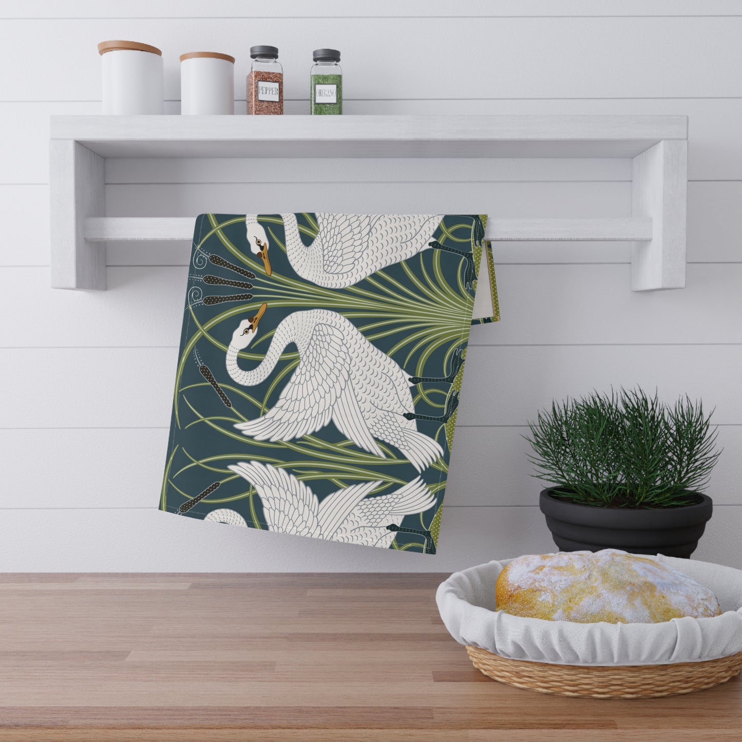 A kitchen tea towel featuring a repeated pattern of a white swan with a green and brownish background, and a set of dishes with cutlery on the side.