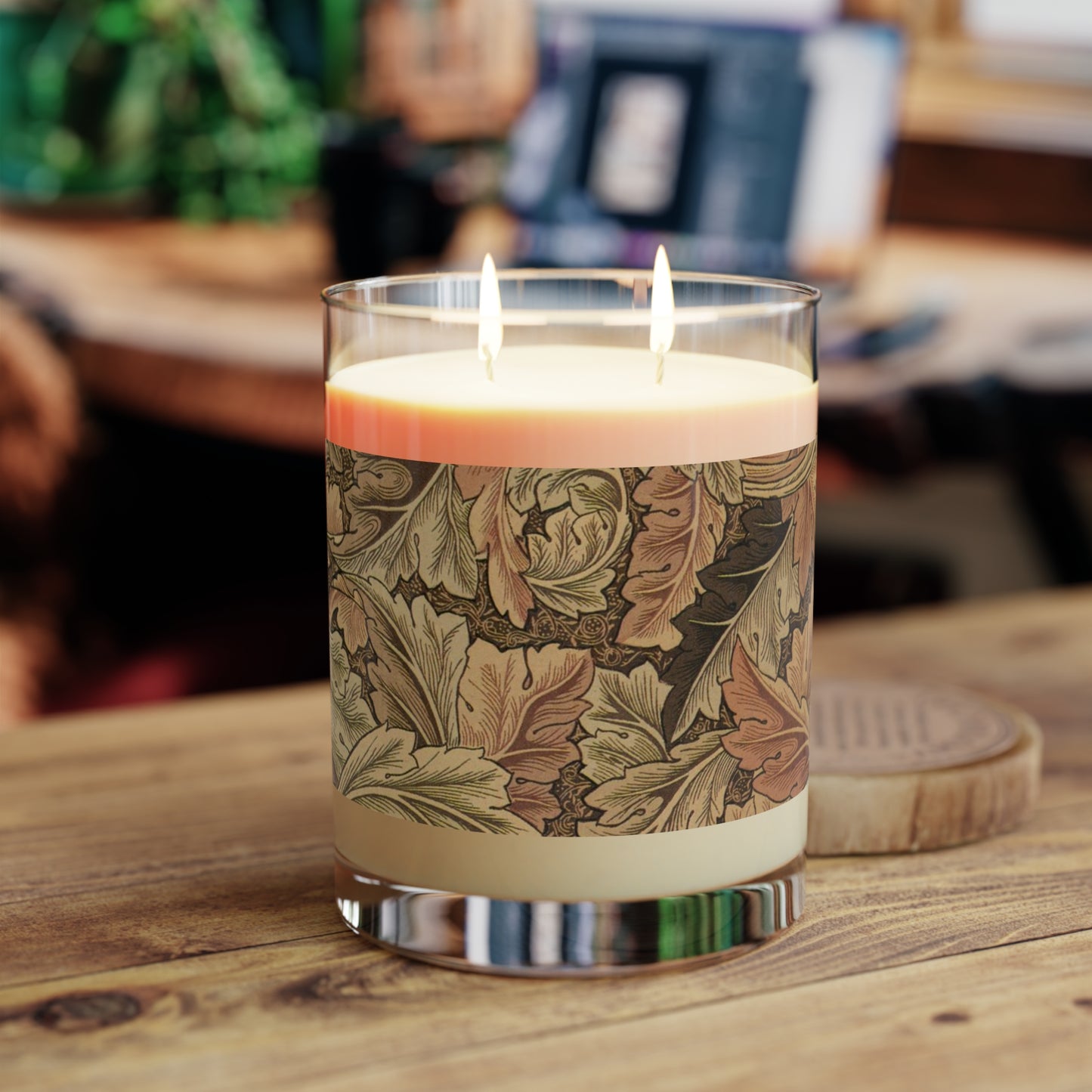 A brown luxury scented candle with a floral William Morris & Co patterned label, alongside a brown cardboard lid with text. The candle is placed in a clear glass jar.