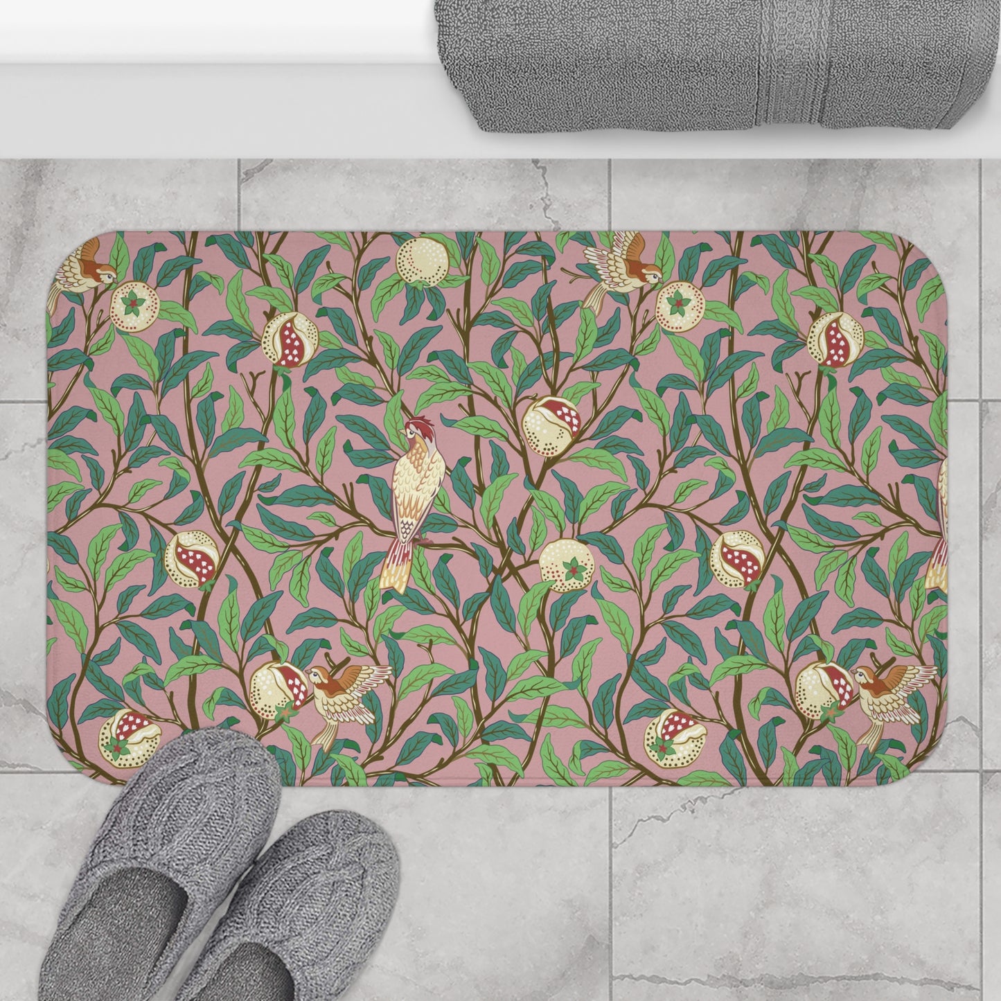 A rectangular microfibre bath mat with a William Morris floral pattern featuring birds and pomegranates in pink, green and white colours.