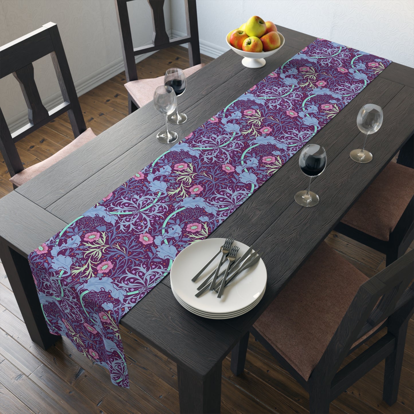 A multicolored table runner with a floral William Morris & Co pattern in pink and green on a blue background, displayed on a table with dishes and cutlery.