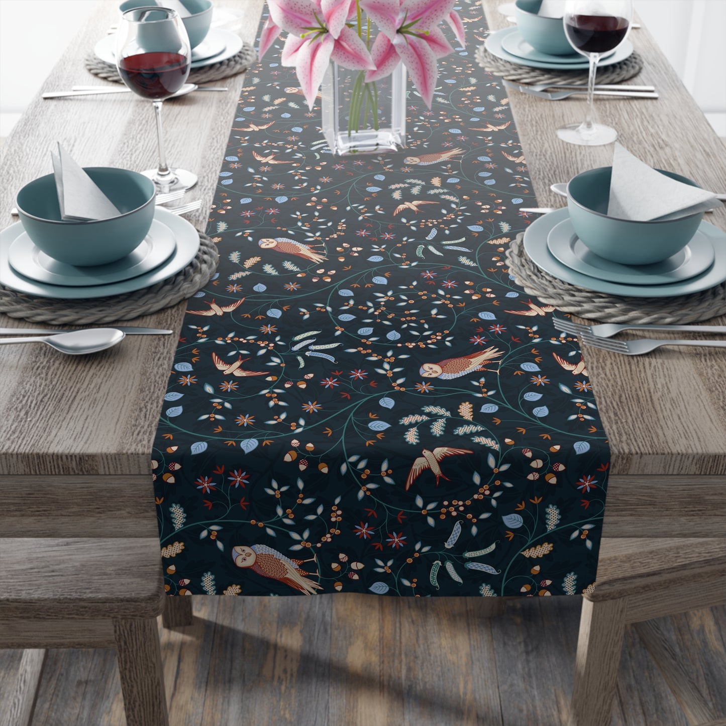 Table setting with a decorative table runner featuring birds and floral patterns on a wooden table.