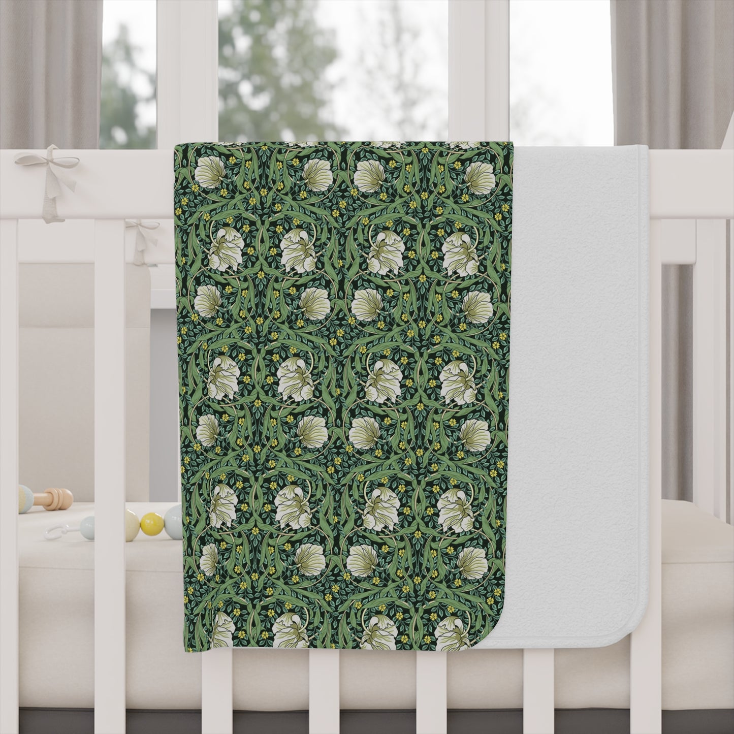 Green floral William Morris & Co Pimpernel patterned toddler blanket draped over a crib