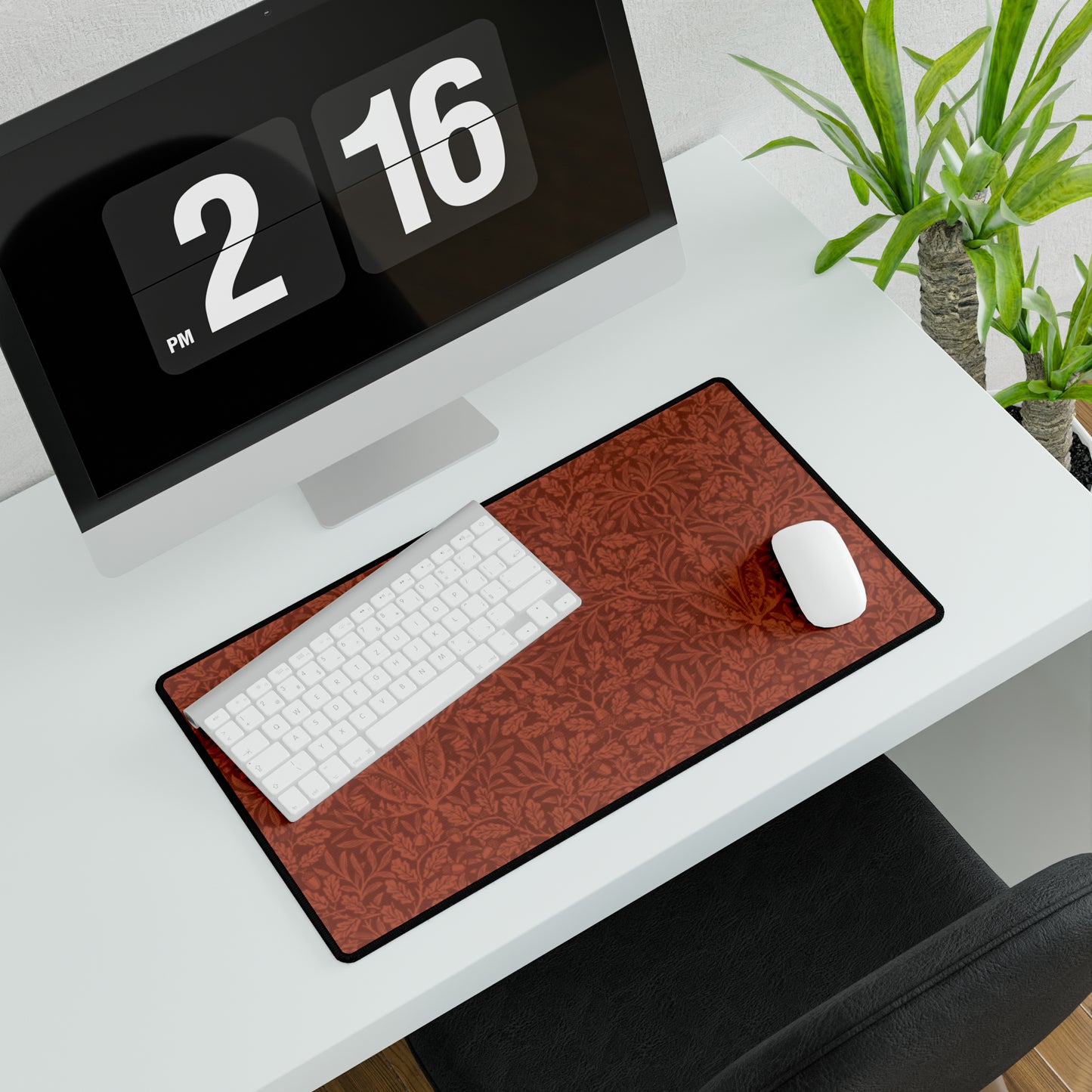 A large desk mat with a floral pattern in brown tones, displayed on a desk with a keyboard and mouse, with a monitor above it showing the time.