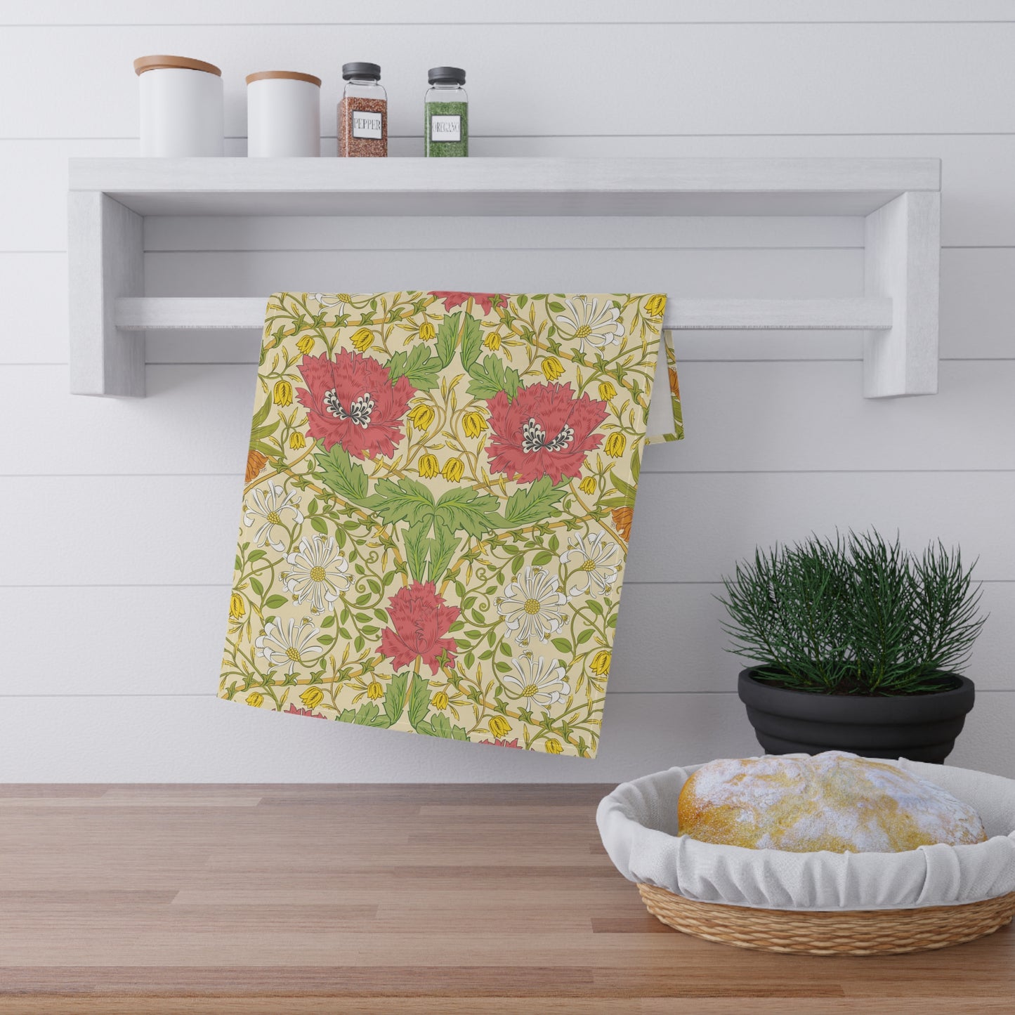 A kitchen tea towel with a floral pattern inspired by William Morris, featuring honeysuckle designs in red, yellow, and green on a light background.