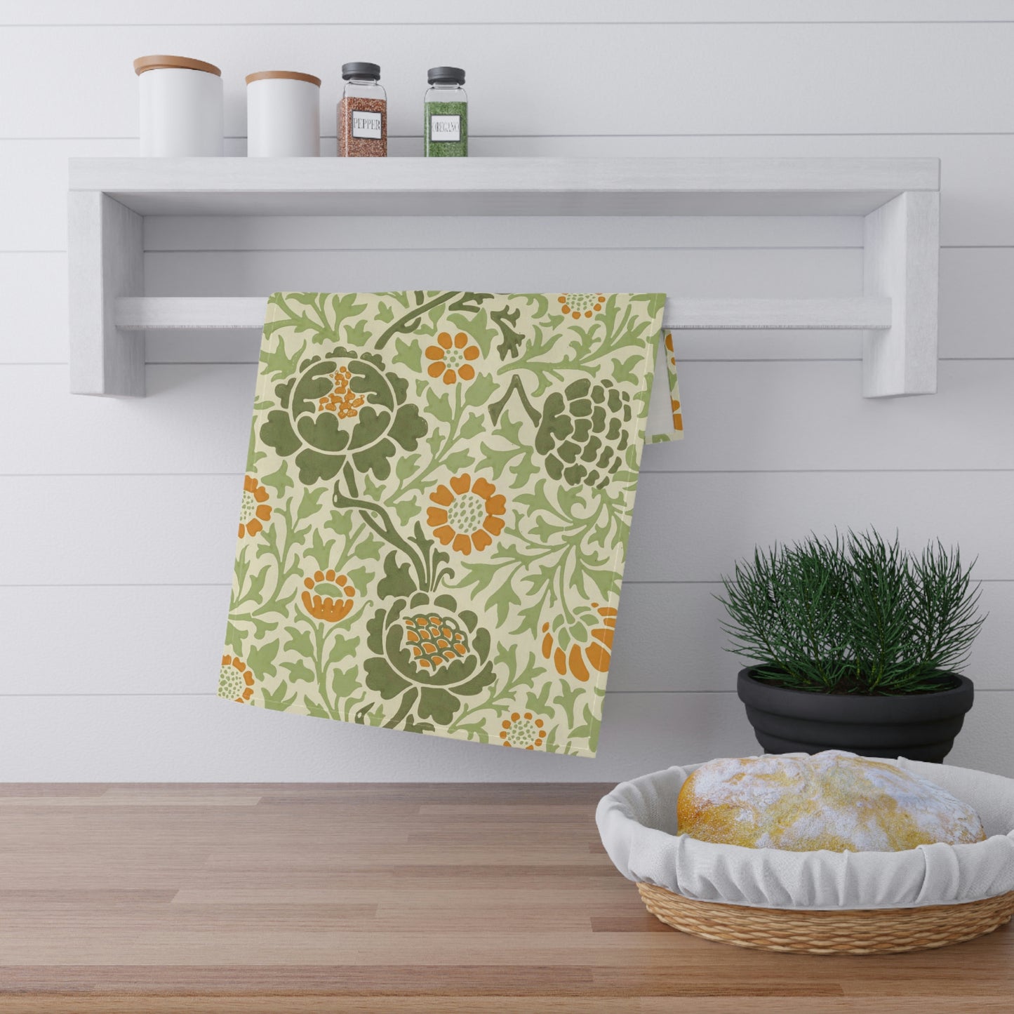A kitchen tea towel with a floral William Morris & Co pattern featuring green, orange and yellow colours on a light background.