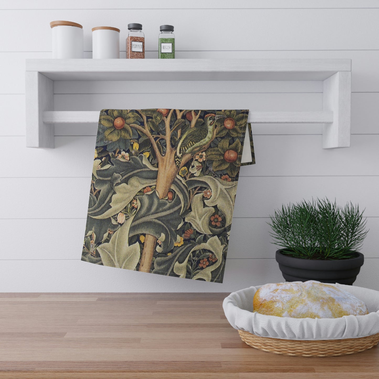 A kitchen tea towel featuring an artistic William Morris & Co design with birds, flowers, and leaves on a green background.