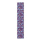 A multicolored table runner with a floral William Morris & Co pattern in pink and green on a blue background, displayed on a table with dishes and cutlery.