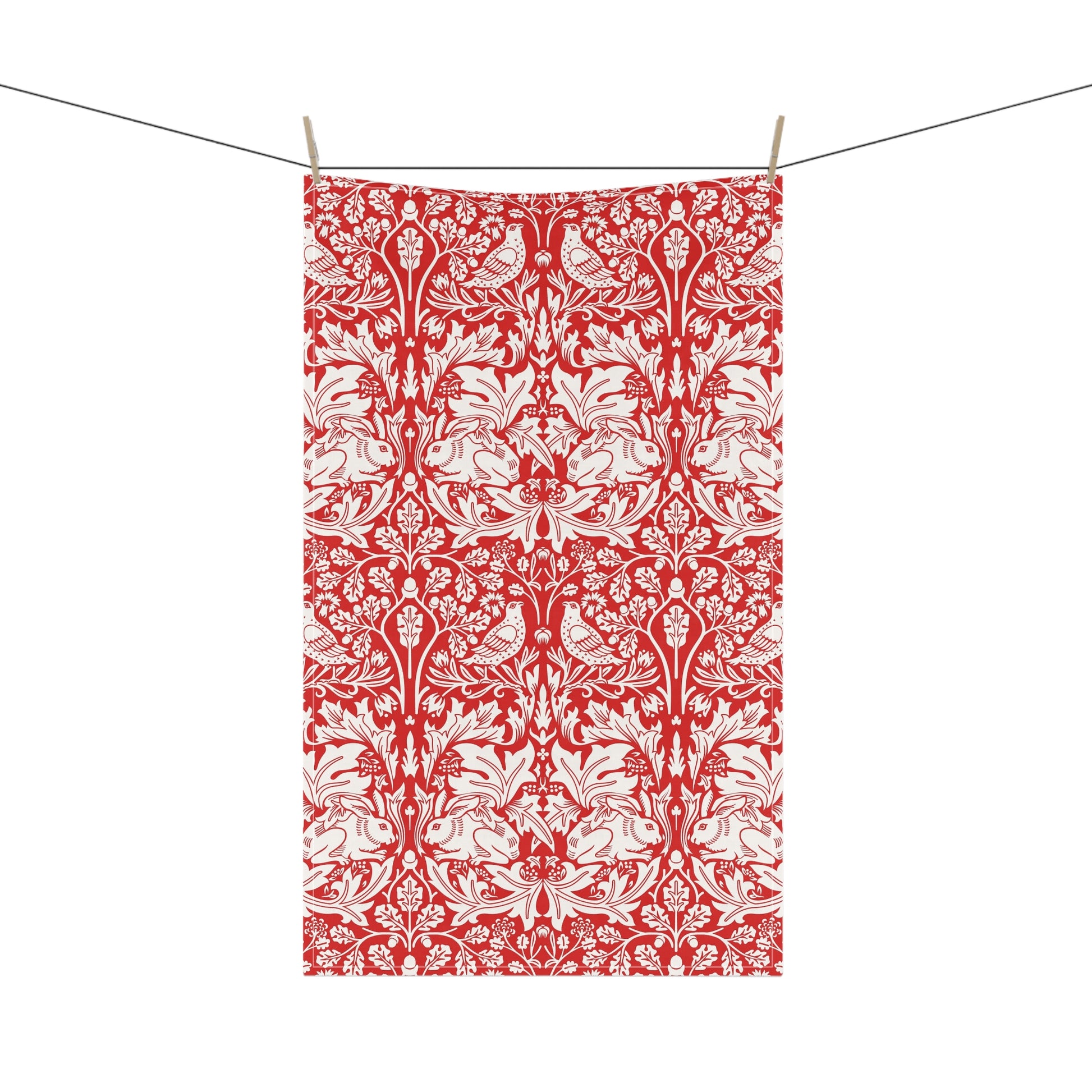 A rectangular tea towel with a red and white ornate floral damask pattern, hanging from a string with three wooden clothespins against a plain white background.
