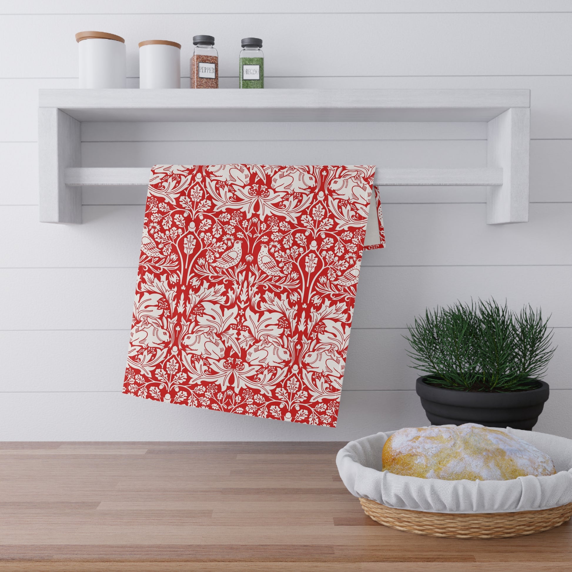 A red and white damask-patterned kitchen towel hanging from a white wall-mounted rack in a bright kitchen setting.