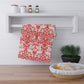 A red and white damask-patterned kitchen towel hanging from a white wall-mounted rack in a bright kitchen setting.