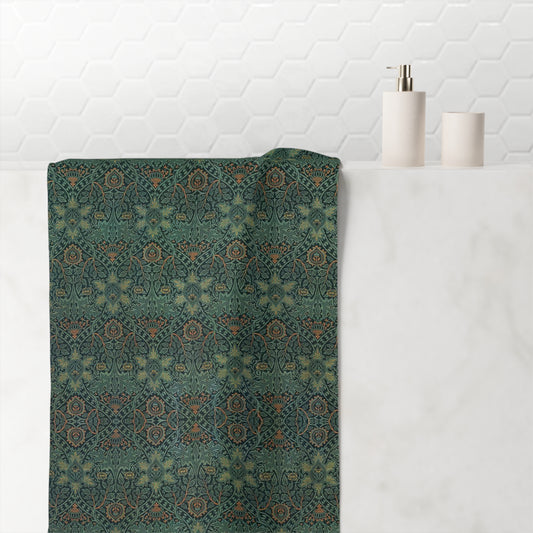 A rectangular bath towel with an intricate, repeating geometric and floral pattern in muted teal, olive green, rust orange, and beige tones, shown flat against a solid white background.