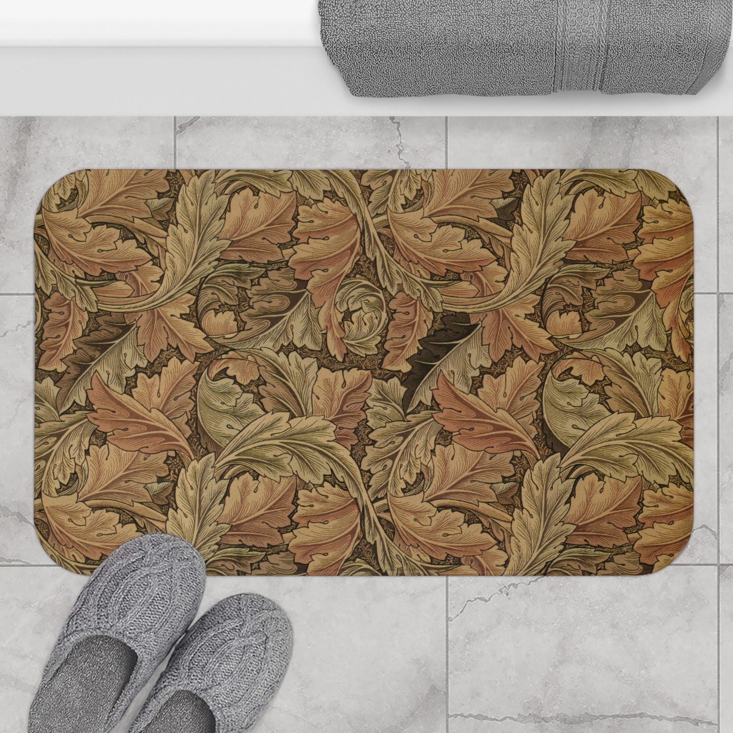 Decorative bath mat with leaf pattern on a marble floor with slippers and towel.