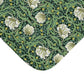 A close-up of a textile or fabric corner showing an allover botanical pattern with large white flowers, green leaves, and small yellow blossoms on a dark green background.