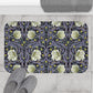 A rectangular microfibre bath mat with a floral pattern in shades of purple and green, inspired by William Morris' design.