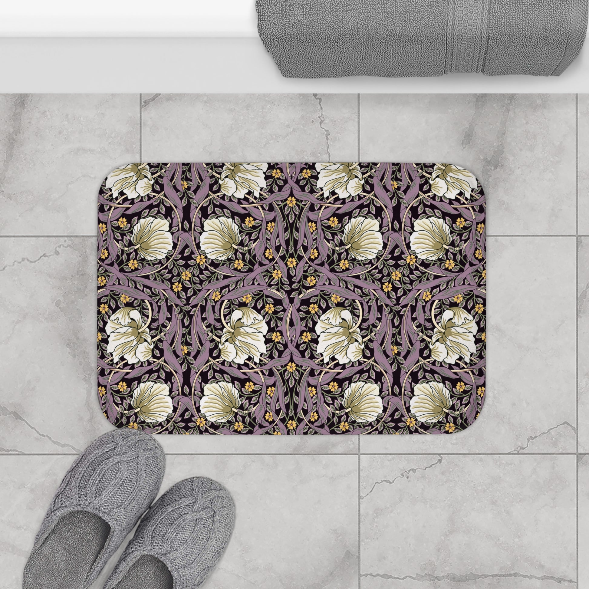 Decorative bathmat with floral pattern on a tiled floor, accompanied by slippers and a towel.