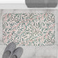 Floral-patterned bath mat on a tiled floor with slippers and a towel.