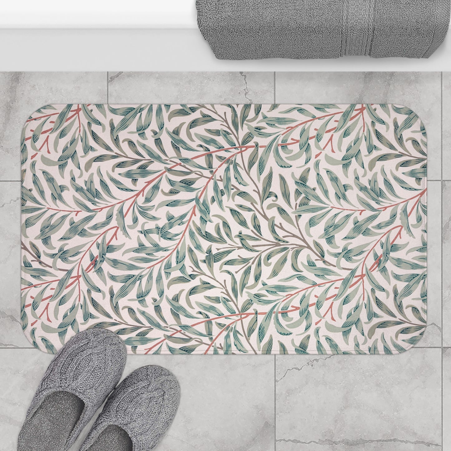 Floral-patterned bath mat on a tiled floor with slippers and a towel.