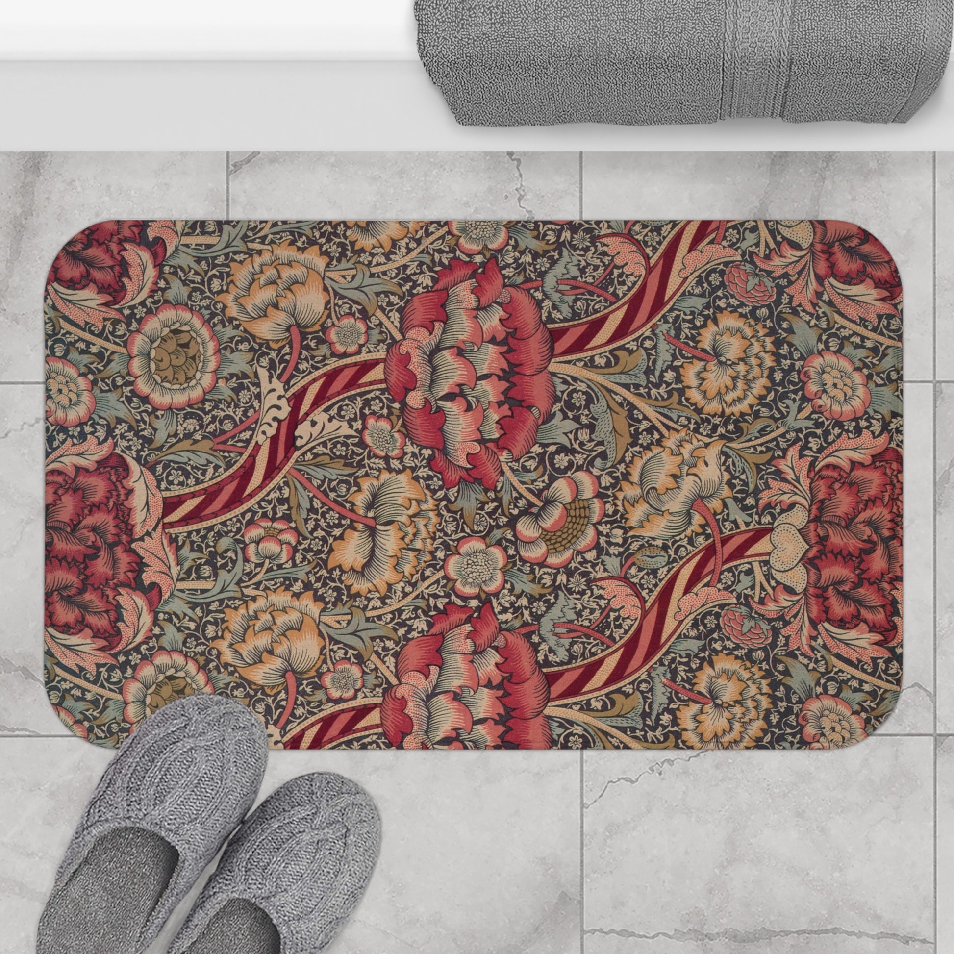 A rectangular microfibre bath mat with a floral pattern inspired by William Morris, predominantly red with a non-slip black border.