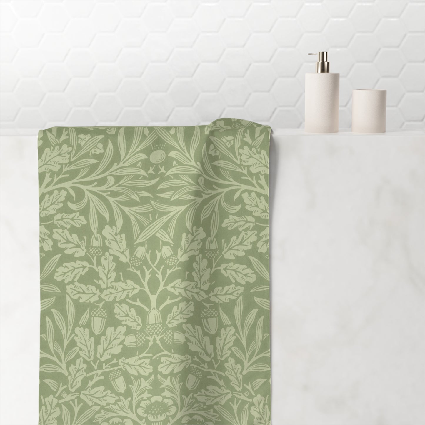 A sage green bath towel with a light beige botanical damask pattern draped over a white marble tub, with a white hexagonal tile wall and minimalist bathroom accessories in the background.