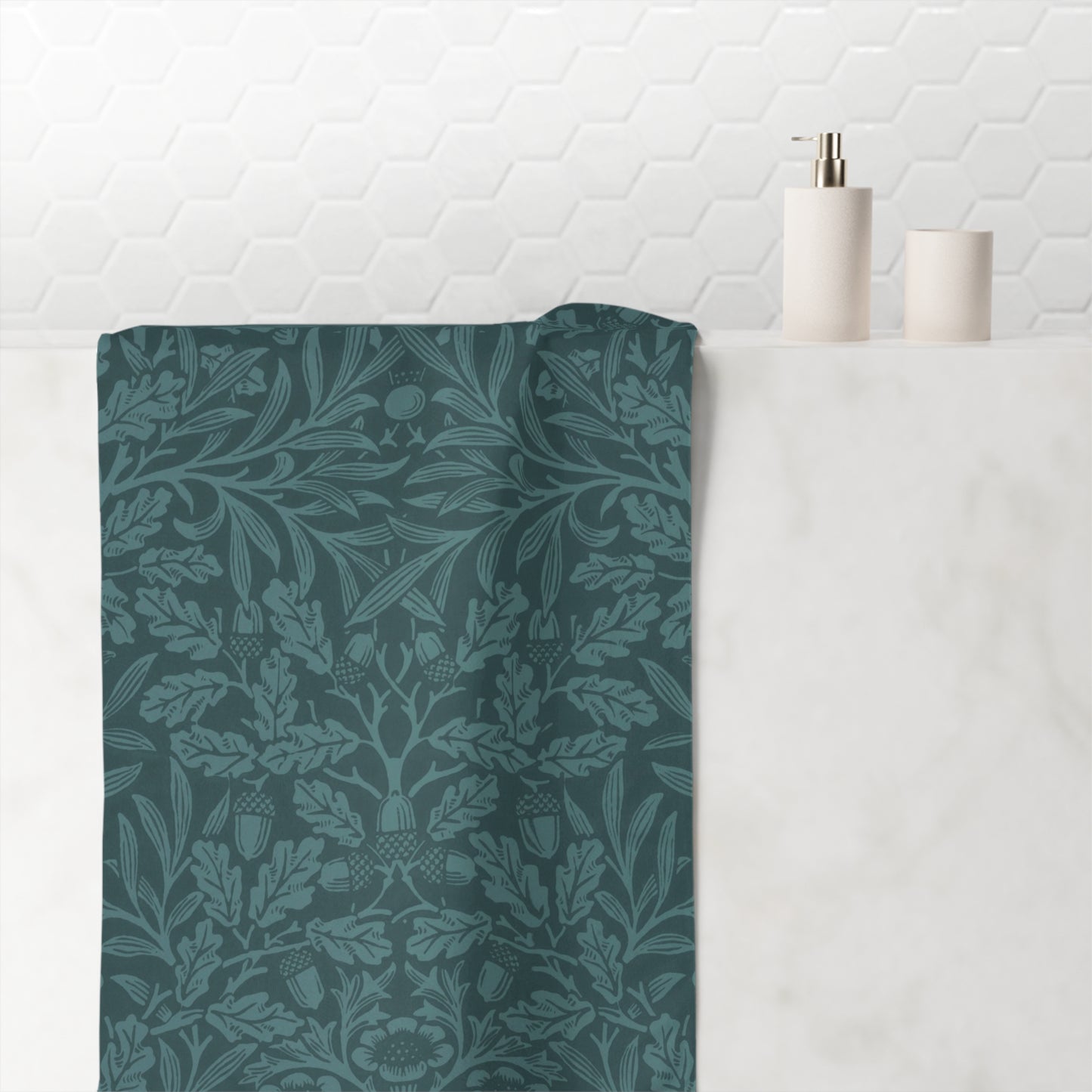A dark teal bathroom towel with a classic William Morris-style floral and botanical damask pattern, draped over a white marble counter next to minimalist white ceramic bathroom accessories.