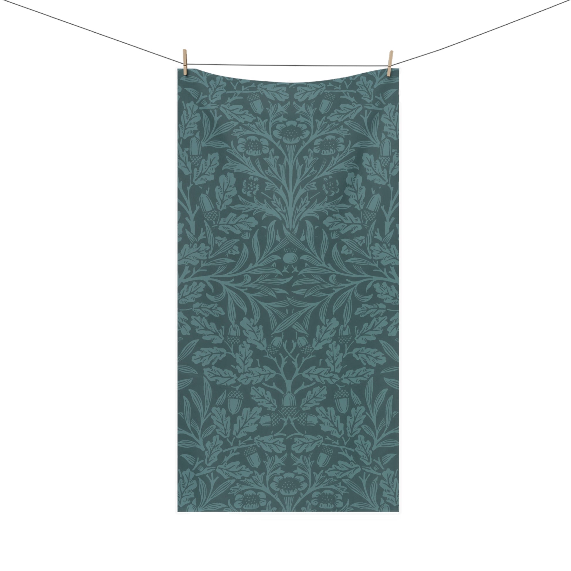 A rectangular bath towel hanging from a clothesline with two wooden clips, featuring an all-over botanical and floral pattern in muted teal and blue-green tones on a white background.