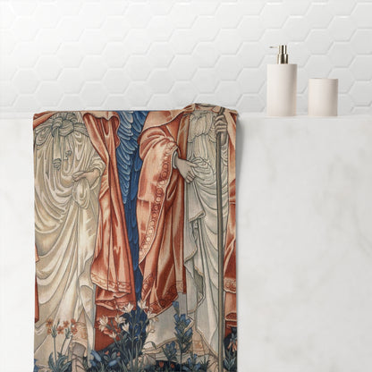 A bathroom towel featuring a vintage-style illustration of cloaked figures in flowing robes, draped over a white marble tub with a white hexagonal tile backsplash and minimalist bathroom accessories in the background.