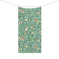 A rectangular bath towel with a repeating botanical and bird pattern, suspended from a string with wooden clips against a plain white background.