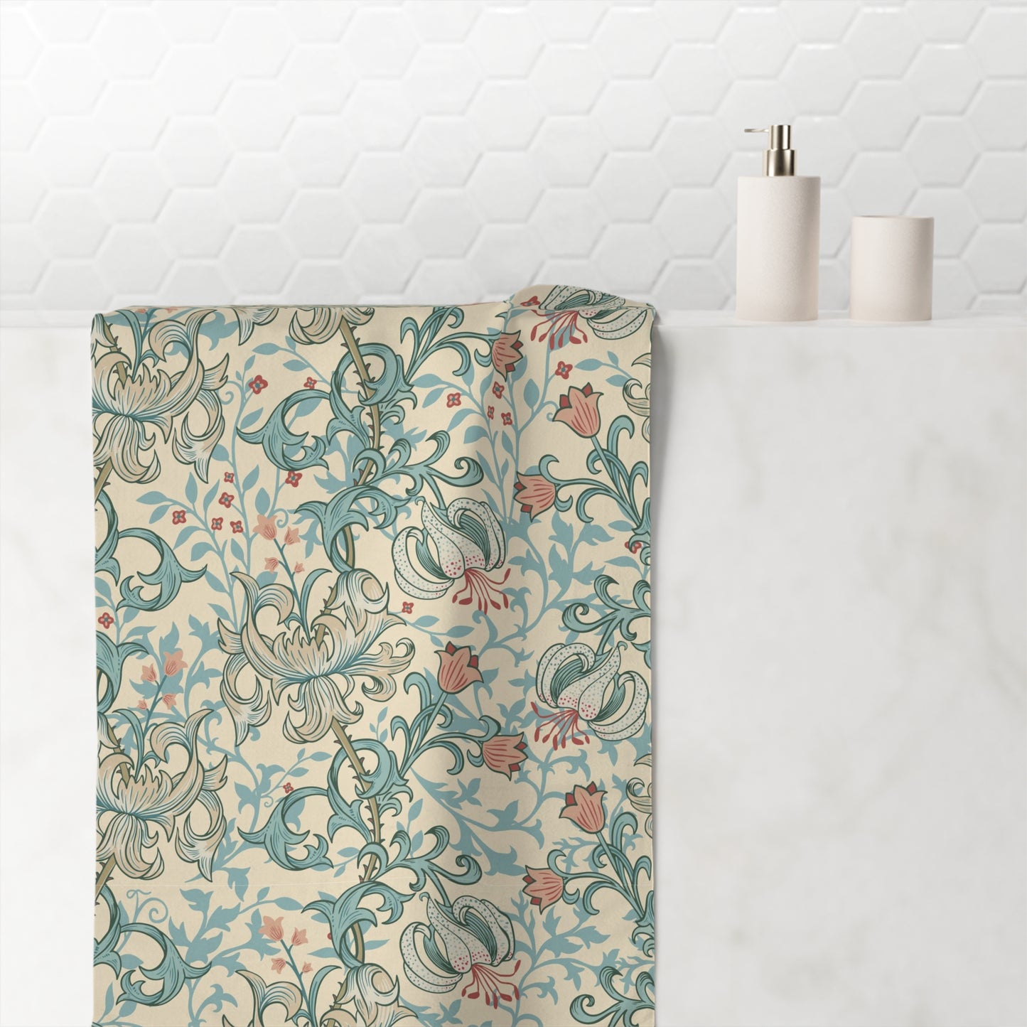 A bathroom towel draped over a white marble counter, featuring a vintage-style floral and scroll pattern in teal, dusty pink, and beige. A white hexagonal tile backsplash is visible in the background, along with minimalist bathroom accessories on the counter.