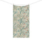 A rectangular fabric towel or scarf with an intricate floral and scroll pattern in teal, dusty pink, and olive green on a cream background, hanging from a clothesline with two wooden clips against a solid white background.