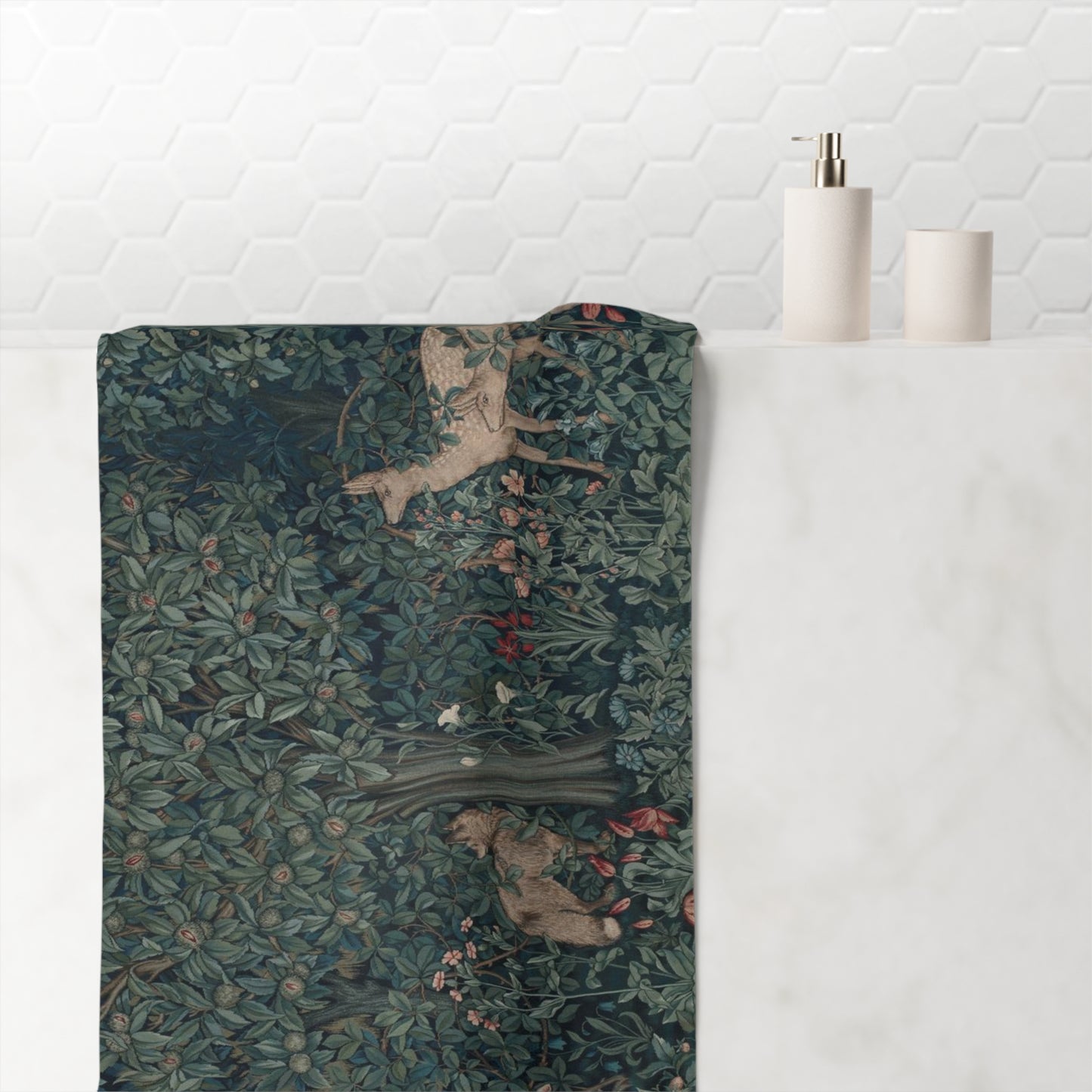 A rectangular bath towel with a detailed William Morris-style woodland print featuring deer and foliage, draped over the edge of a white marble bathroom counter next to a white tiled wall.