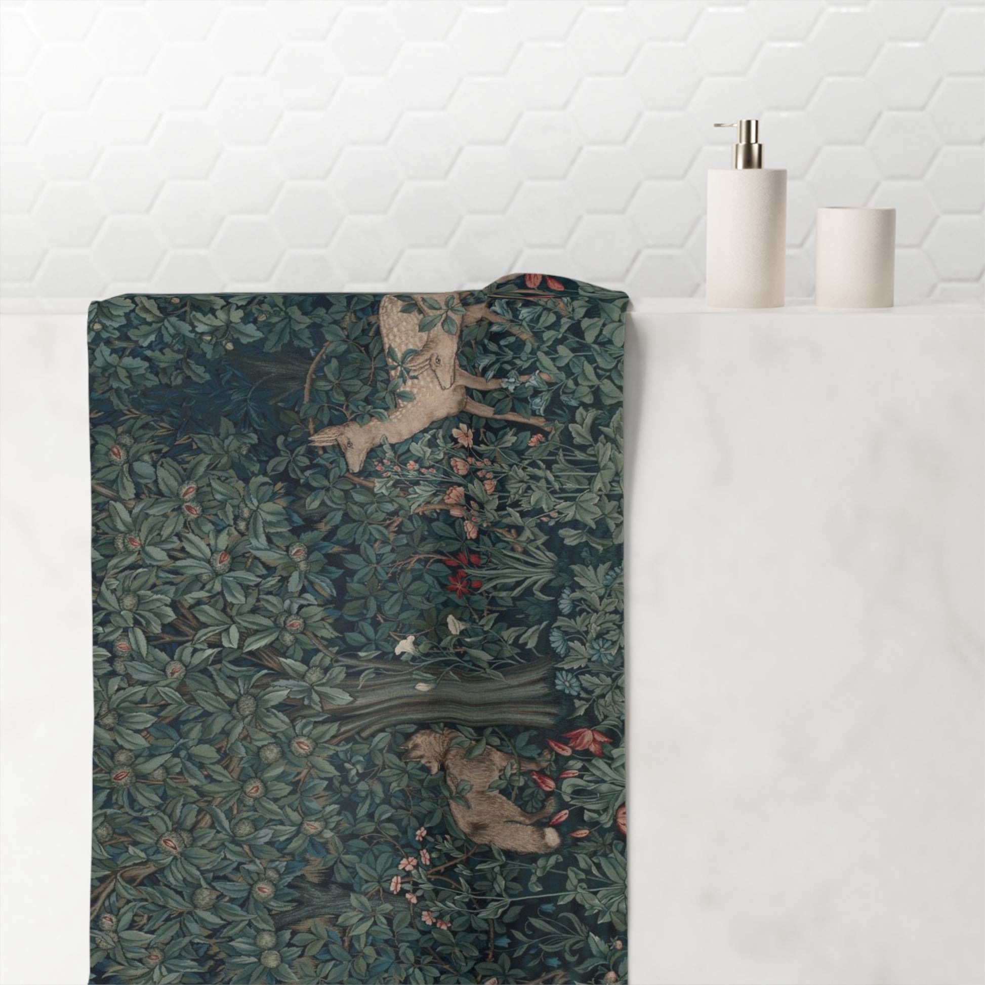 A rectangular bath towel with a detailed William Morris-style woodland print featuring deer and foliage, draped over the edge of a white marble bathroom counter next to a white tiled wall.