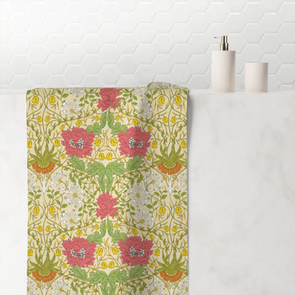 A decorative bath towel draped over the edge of a white marble bathtub, featuring a vintage-style floral and botanical pattern with pink flowers, green leaves, and yellow accents on a cream background. A white hexagonal tile wall and minimalist bathroom accessories are visible in the background.