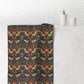A bathroom towel draped over a white marble tub edge, featuring a dense floral and bird pattern on a dark background. The pattern includes orange birds, pink flowers, and green foliage.