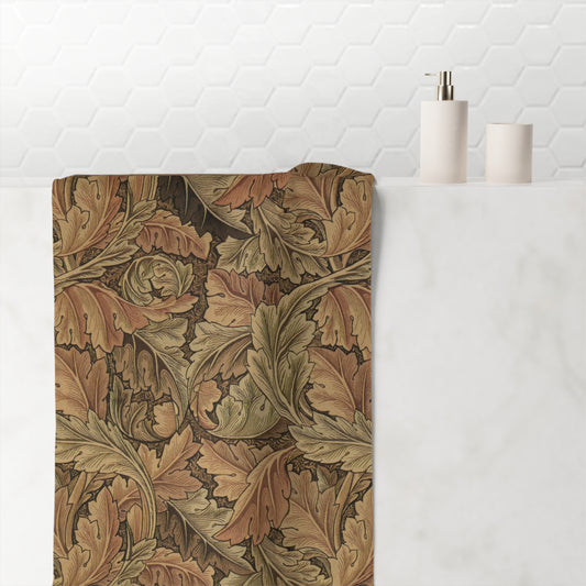 A rectangular bath mat with an intricate William Morris-style oak leaf pattern in earthy brown, beige, and muted green tones, styled on a white marble bathroom counter next to minimalist white toiletries against a white hexagonal tile wall.