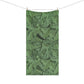 A rectangular beach towel with a green and dark green acanthus leaf pattern, hanging from a clothesline with two wooden clips against a solid white background.