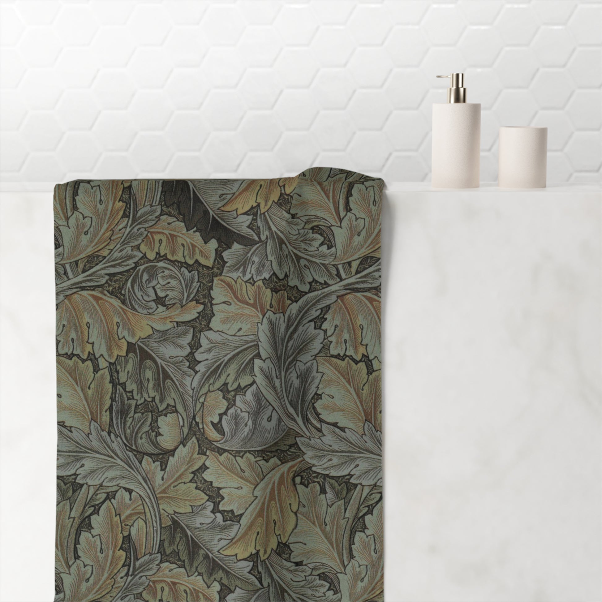 A rectangular bath mat with an intricate William Morris-style acanthus leaf pattern in muted gray, olive green, and beige tones, styled on a white marble countertop next to minimalist white bathroom accessories against a white hexagonal tile wall.