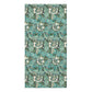 A bath towel with a detailed botanical pattern in teal, green, and white hangs over the edge of a white marble bathroom counter. In the background, a white hexagonal tiled wall is visible, along with a white pump dispenser and a small white cup.
