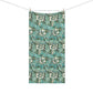 A bath towel with a detailed botanical pattern in teal, green, and white hangs over the edge of a white marble bathroom counter. In the background, a white hexagonal tiled wall is visible, along with a white pump dispenser and a small white cup.