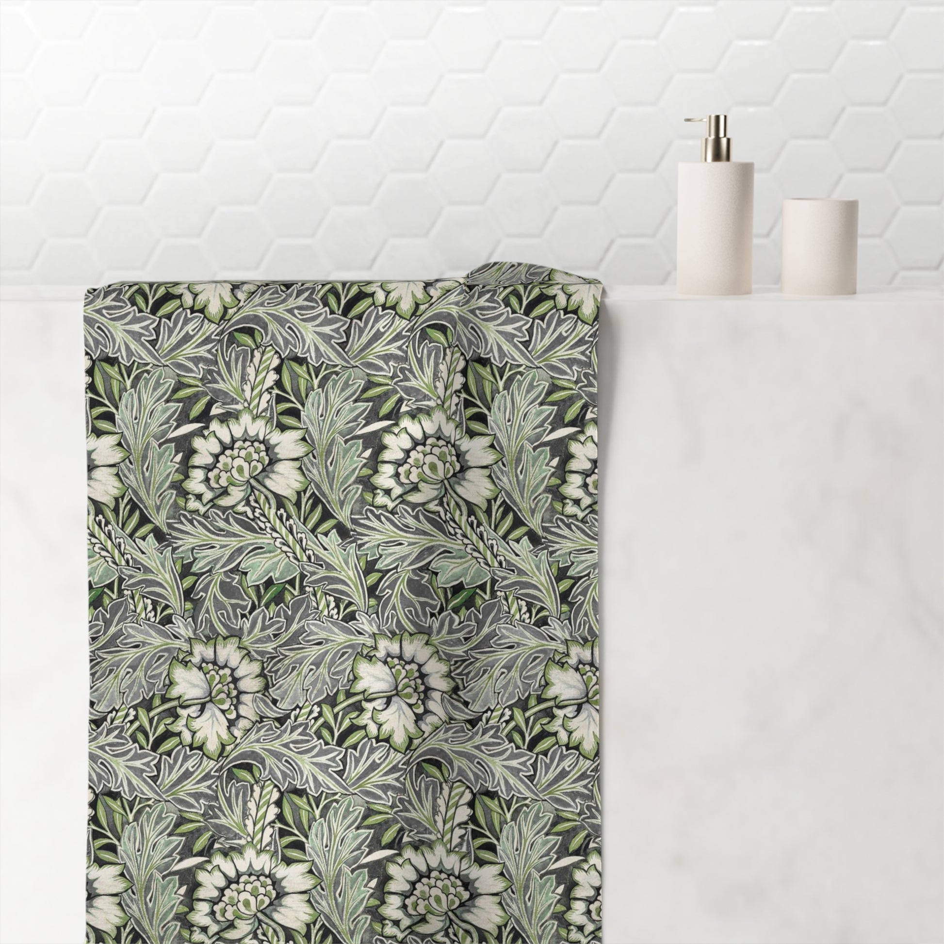 A bathroom towel with a detailed botanical pattern in shades of green, gray, and white, draped over a white marble counter next to minimalist white bathroom accessories.